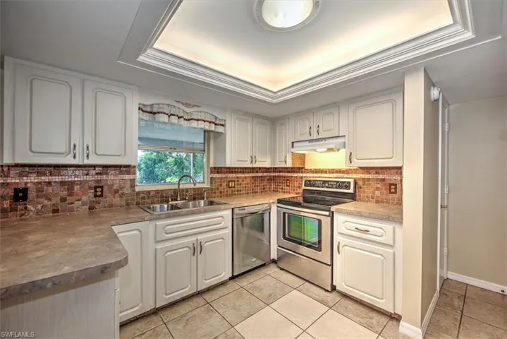 Kitchen with backsplash, appliances with stainless steel finishes, sink, and a raised ceiling