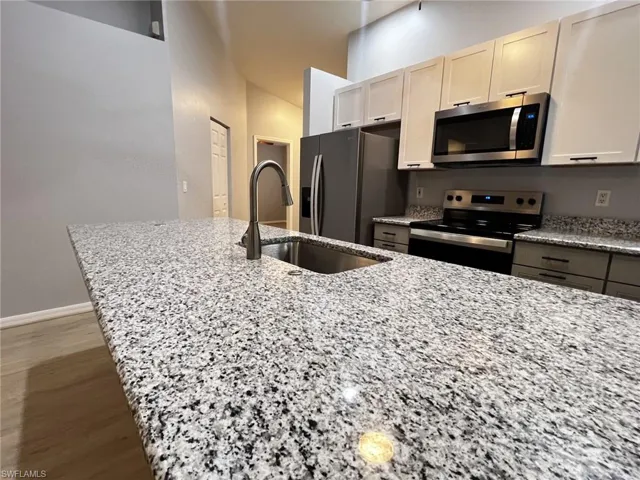 Kitchen featuring light stone counters, stainless steel appliances, and wood finished floors