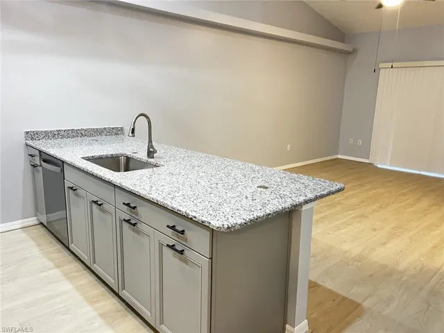 Kitchen with gray cabinets, light stone countertops, a peninsula, light wood-style flooring, and vaulted ceiling