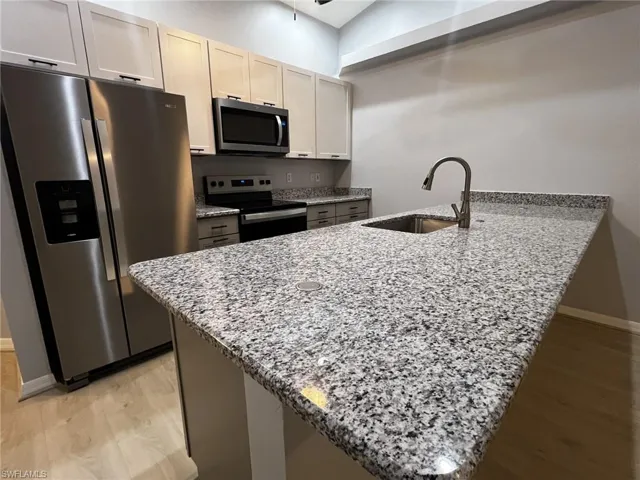 Kitchen featuring light stone countertops, stainless steel appliances, a peninsula, and light wood finished floors