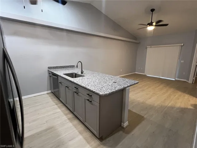 Kitchen with ceiling fan, a peninsula, light stone countertops, light wood-style floors, and vaulted ceiling