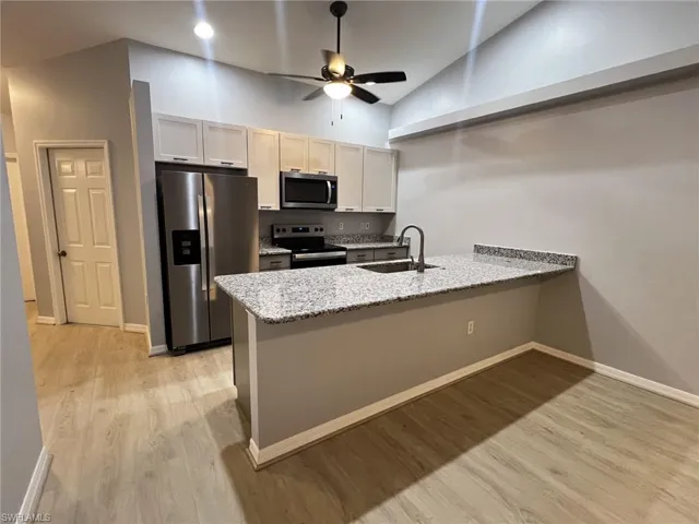 Kitchen featuring stainless steel appliances, light stone counters, a peninsula, light wood-type flooring, and lofted ceiling