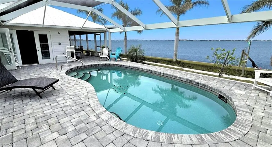 Outdoor pool featuring a patio, a sunroom, glass enclosure, and a water view
