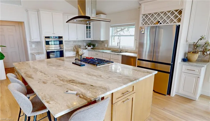 Kitchen with stainless steel appliances, light stone countertops, a breakfast bar, and island exhaust hood