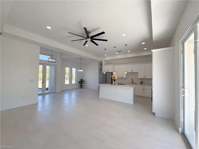 Kitchen with white cabinetry, ceiling fan, a center island with sink, tasteful backsplash, and open floor plan