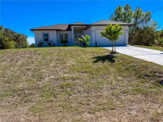 View of front facade featuring a front yard, stucco siding, concrete driveway, an attached garage, and french doors