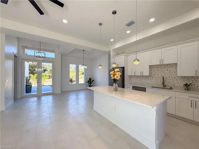 Kitchen with white cabinetry, stainless steel appliances, light stone countertops, tasteful backsplash, and a center island