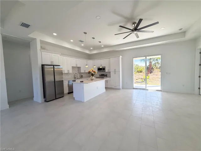 Kitchen featuring stainless steel appliances, open floor plan, white cabinetry, a center island, and a raised ceiling