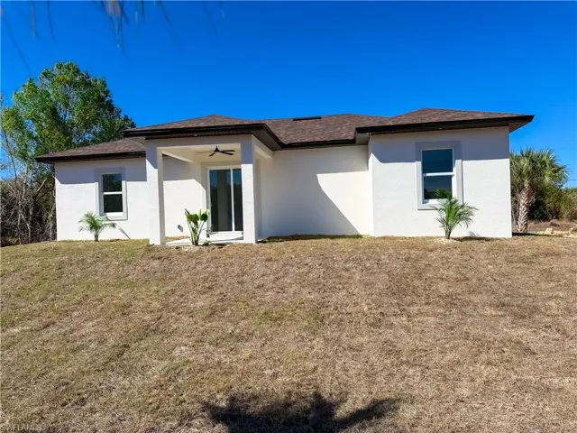 Rear view of property with stucco siding, a yard, a shingled roof, and a ceiling fan
