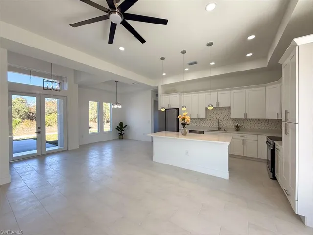 Kitchen with decorative backsplash, white cabinetry, a kitchen island, black range with electric cooktop, and freestanding refrigerator