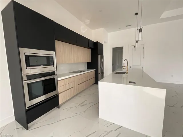 Kitchen with sink, appliances with stainless steel finishes, hanging light fixtures, an island with sink, and light brown cabinets