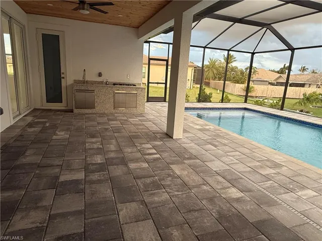 View of pool featuring ceiling fan, an outdoor kitchen, glass enclosure, and a patio area