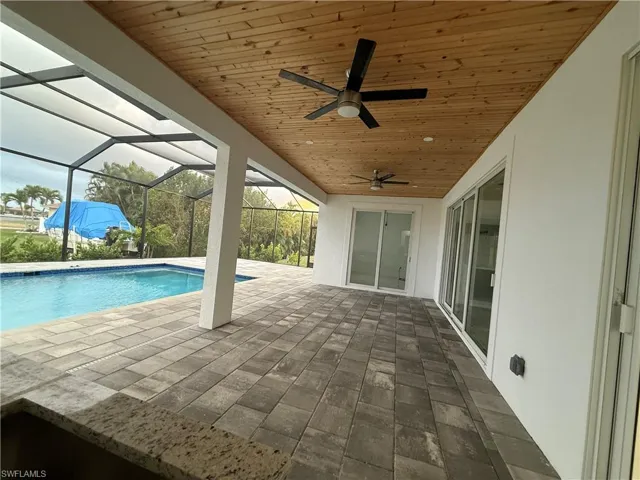View of swimming pool featuring a patio area, ceiling fan, and glass enclosure