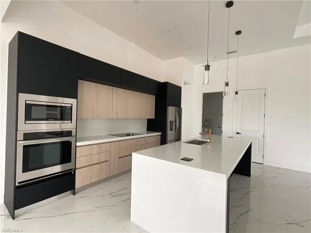 Kitchen featuring sink, appliances with stainless steel finishes, a kitchen island with sink, decorative light fixtures, and light brown cabinets