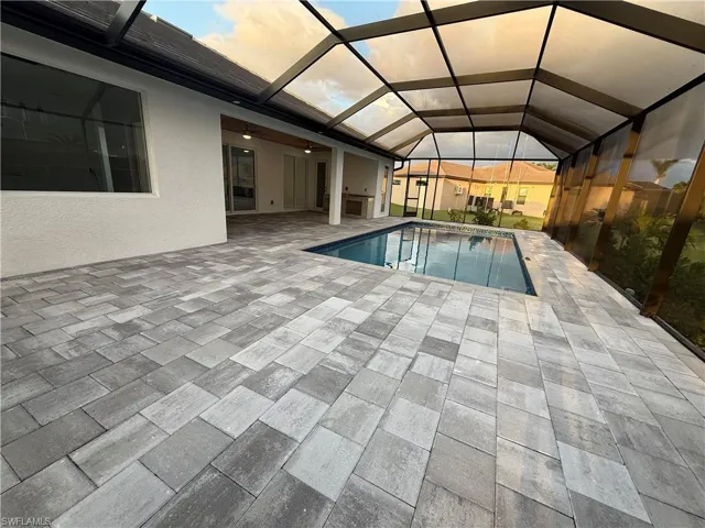 Pool at dusk featuring a patio, ceiling fan, and glass enclosure