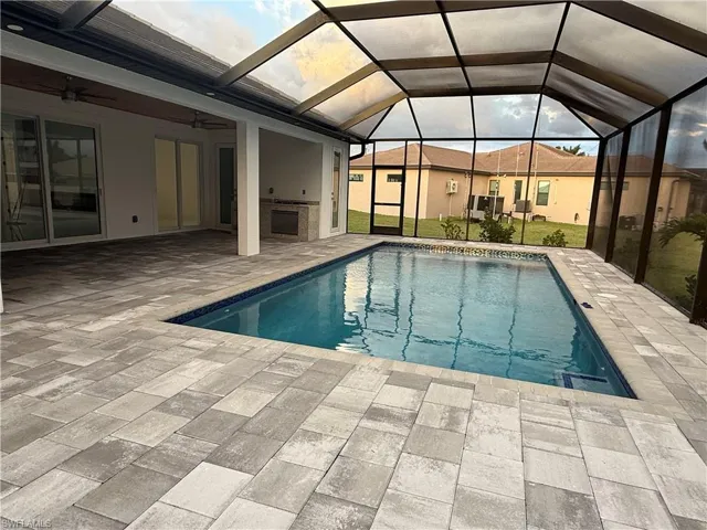 View of swimming pool with a lanai, a patio, ceiling fan, and an outdoor kitchen