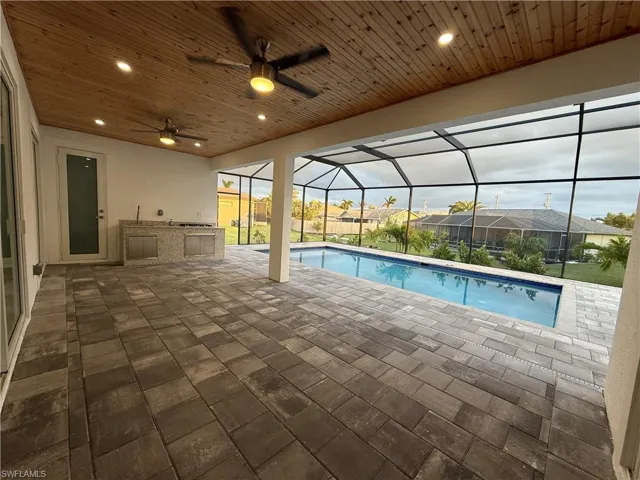 View of swimming pool with ceiling fan, area for grilling, glass enclosure, and a patio