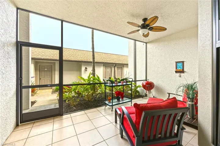 Sunroom with a textured wall, a ceiling fan, a textured ceiling, a wall of windows, and tile patterned flooring