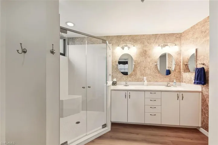 Full bathroom with a shower stall, double vanity, light wood finished floors, and tile walls