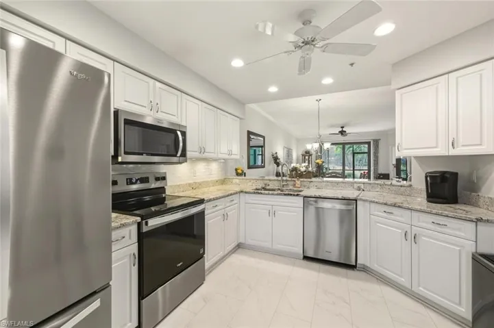 Kitchen with appliances with stainless steel finishes, white cabinets, light stone counters, recessed lighting, and ornamental molding