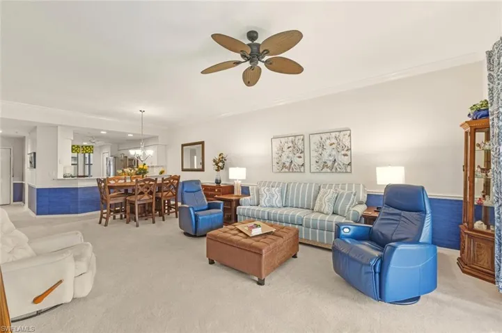 Carpeted living room with ornamental molding, ceiling fan, and wainscoting