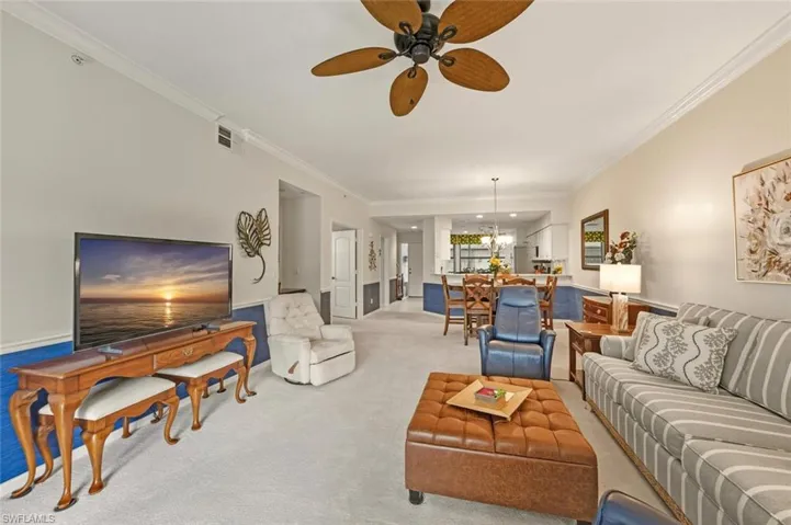 Living room featuring ceiling fan, crown molding, carpet flooring, and a chandelier