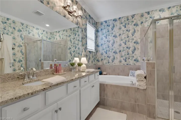 Bathroom featuring double vanity, a shower stall, a bath, wallpapered walls, and ornamental molding