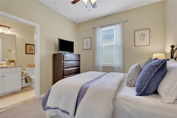 Bedroom with a ceiling fan, light carpet, and ensuite bath