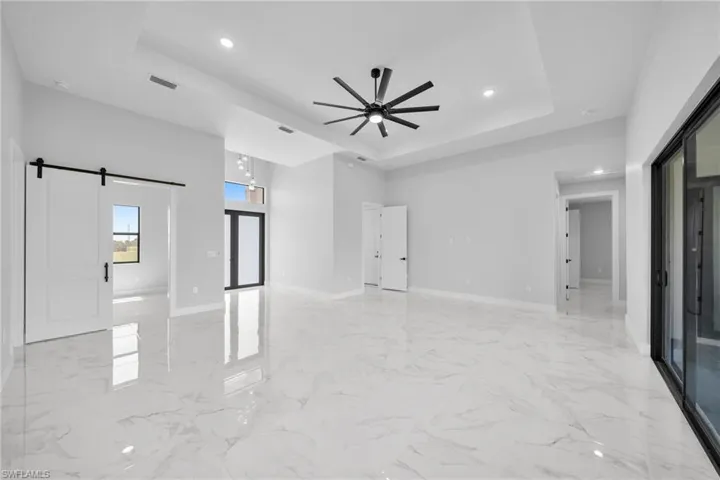 Living room featuring light tile floors, a barn door, ceiling fan, and a raised ceiling