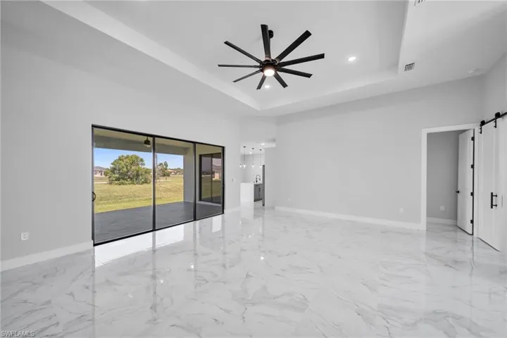 Empty room featuring a barn door, a raised ceiling, ceiling fan, and light tile floors