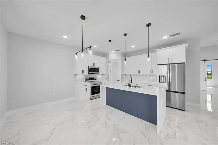 Kitchen featuring stainless steel appliances, white cabinetry, a barn door, sink, and light tile floors