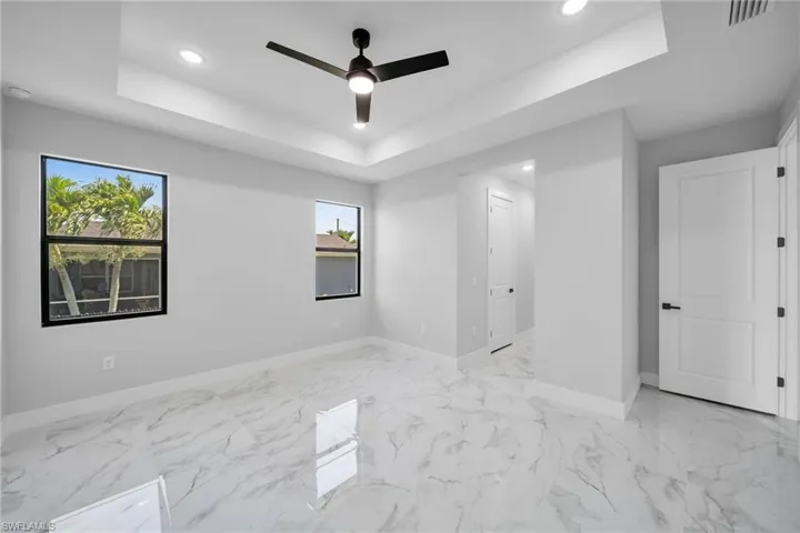 Spare room featuring ceiling fan, light tile floors, and a raised ceiling
