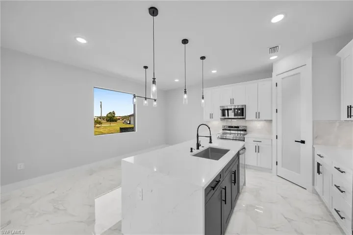 Kitchen with an island with sink, appliances with stainless steel finishes, white cabinets, sink, and light tile floors