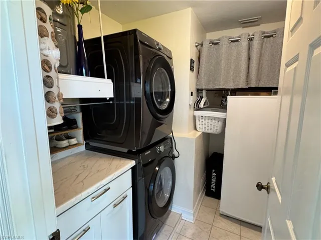 Washroom with cabinet space, light tile patterned flooring, and stacked washer / dryer