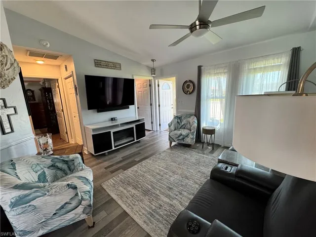 Living room with a ceiling fan, vaulted ceiling, wood finished floors, and visible vents