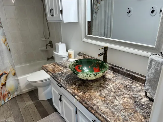 Bathroom with vanity, toilet, wood finished floors, and shower / bath combo with shower curtain