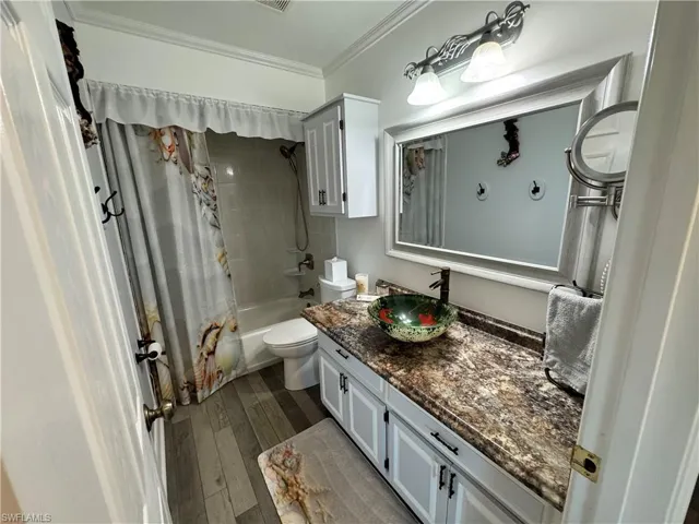 Bathroom with crown molding, shower / bath combo with shower curtain, toilet, hardwood / wood-style floors, and vanity