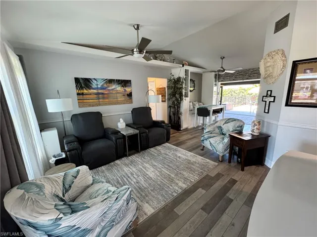 Living room featuring vaulted ceiling, wood finished floors, visible vents, and ceiling fan