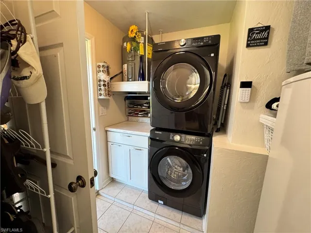 Laundry room with stacked washer / dryer, light tile patterned floors, cabinet space, and a textured wall