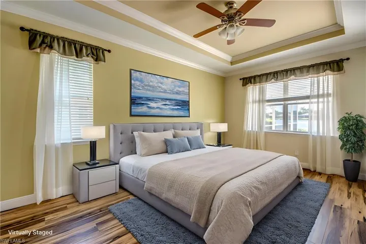 Bedroom featuring a tray ceiling, ornamental molding, wood finished floors, and ceiling fan