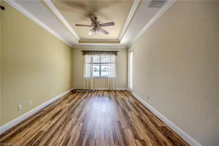 Empty room with a raised ceiling, wood finished floors, a ceiling fan, and ornamental molding