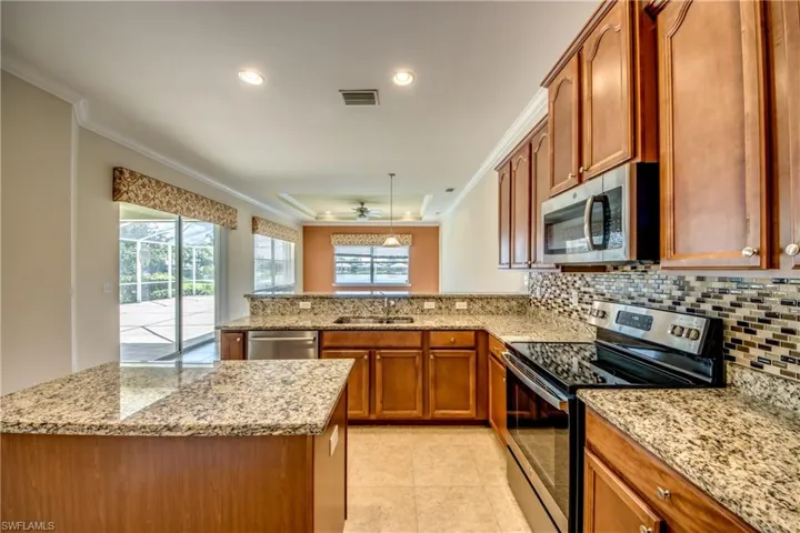 Kitchen featuring stainless steel appliances, a peninsula, brown cabinetry, backsplash, and crown molding
