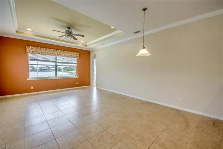 Empty room featuring a tray ceiling, ceiling fan, light tile patterned flooring, crown molding, and recessed lighting