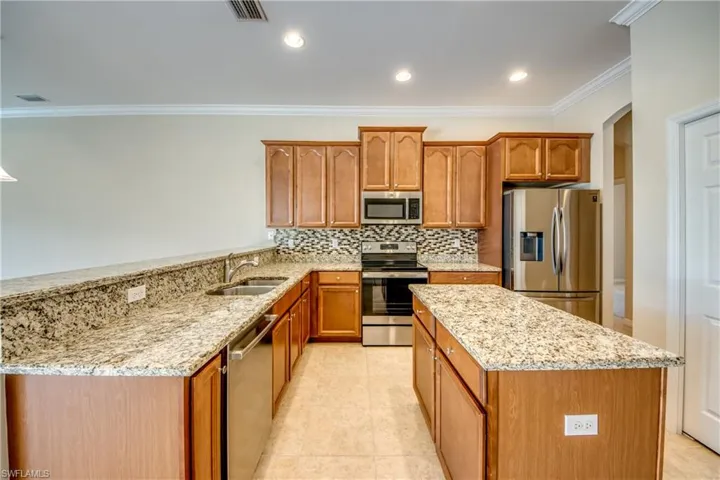 Kitchen with stainless steel appliances, ornamental molding, tasteful backsplash, light stone counters, and a peninsula