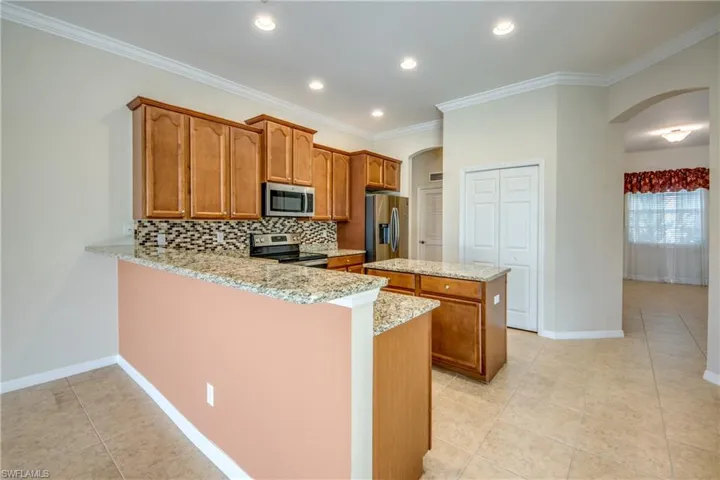 Kitchen featuring arched walkways, stainless steel appliances, a kitchen island, brown cabinets, and light tile patterned floors