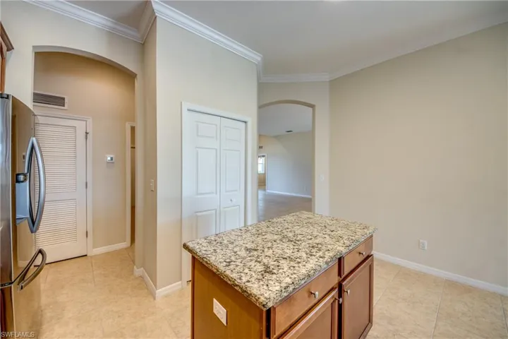 Kitchen with arched walkways, smart refrigerator, light stone counters, light tile patterned flooring, and crown molding