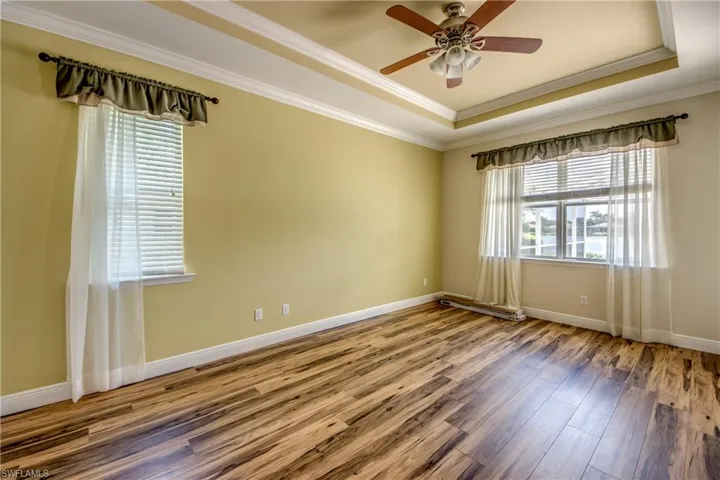 Empty room with a tray ceiling, crown molding, wood finished floors, and a ceiling fan
