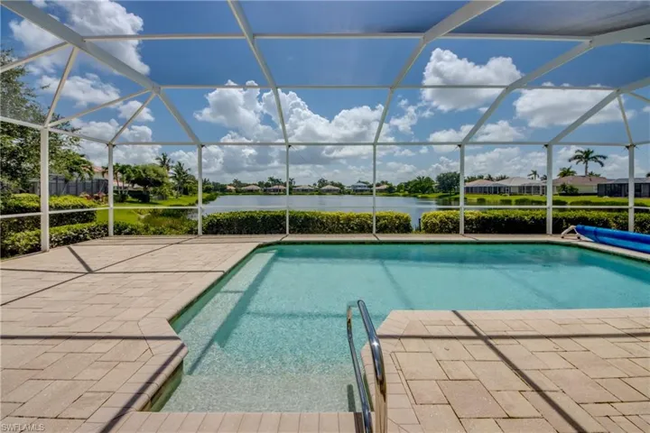 View of swimming pool featuring a water view, a covered pool, a patio, and glass enclosure