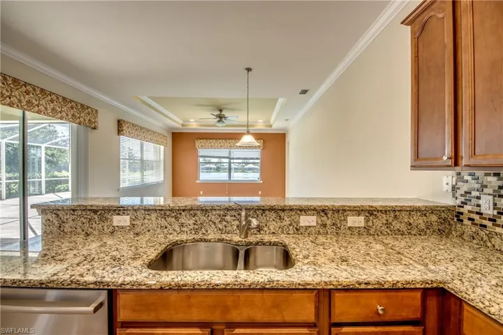 Kitchen with stainless steel dishwasher, ceiling fan, a tray ceiling, light stone counters, and crown molding