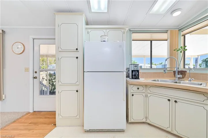 Kitchen with freestanding refrigerator, light countertops, crown molding, decorative backsplash, and white cabinetry